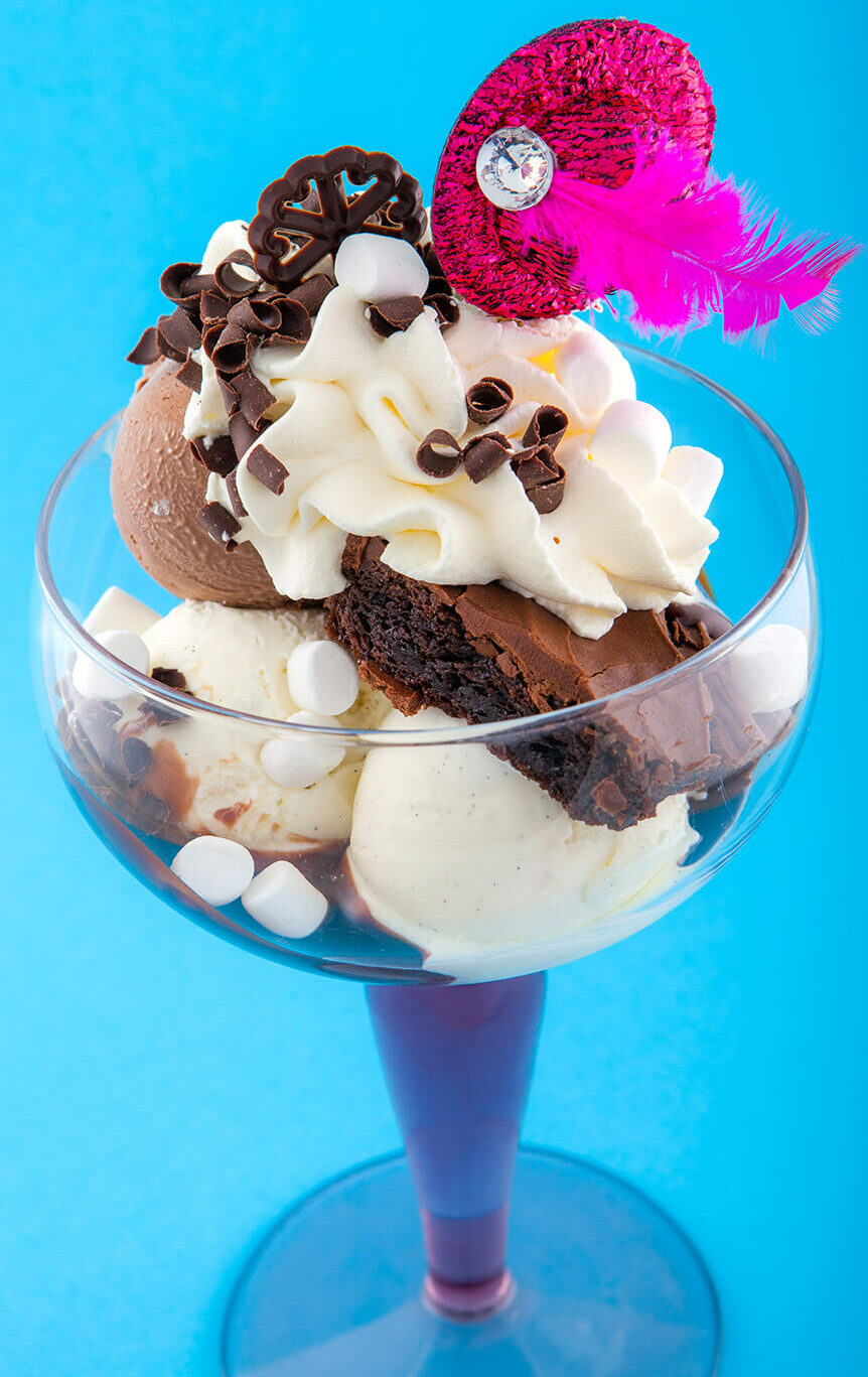 Vanilj- och brownieglass med browniekaka och varm fudge. Toppas med grädde, marshmallows och choklad. Dekoreras med en liten hatt med fjäder.
